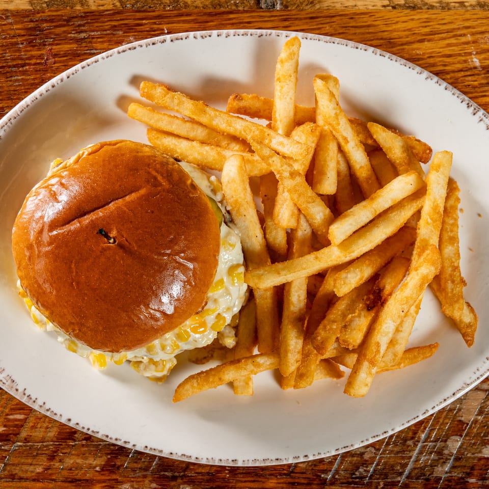 El Camino's burger with creamy corn and a side of golden french fries on a white plate.