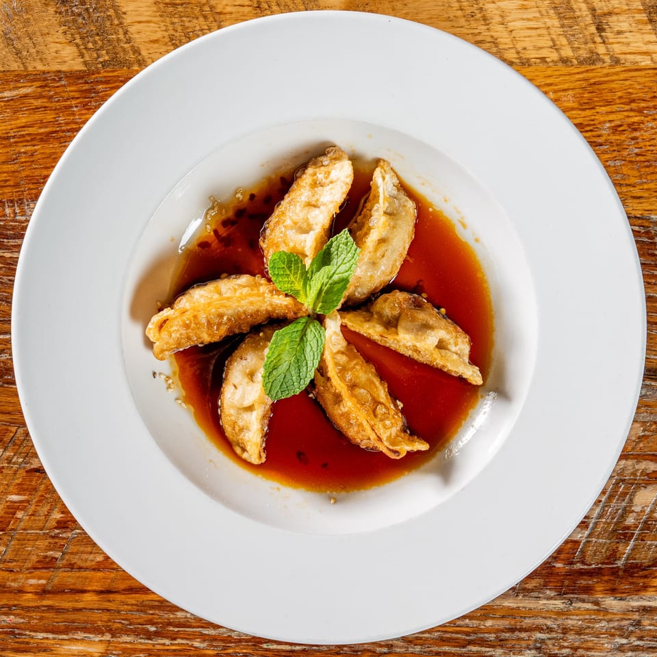 Fried dumplings arranged in a circle with a mint garnish, swimming in a sweet and savory sauce.