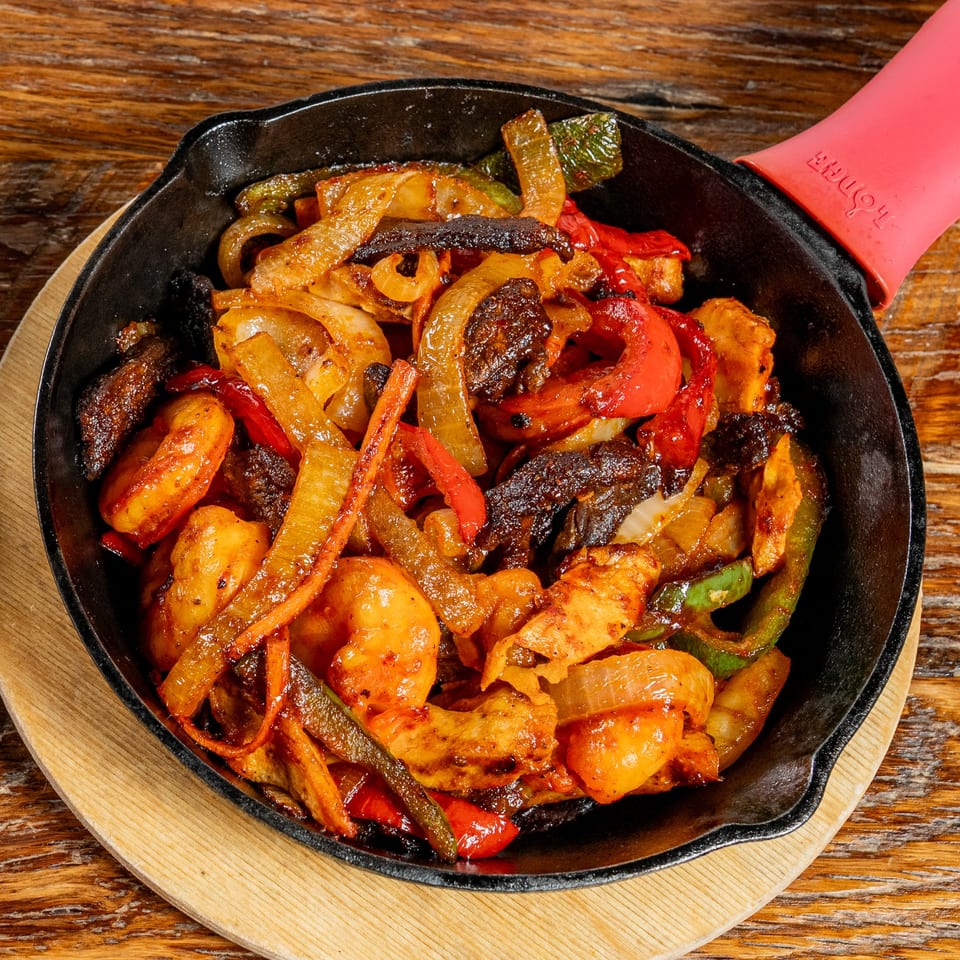Sizzling El Camino fajitas with chicken, shrimp, peppers, and onions in a cast iron skillet.
